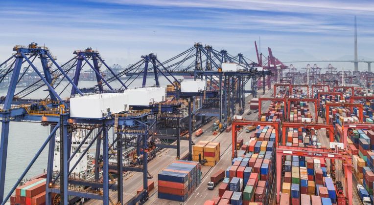 Terminal Operations with Modern Crane Technology Panorama view of a container terminal with rows of containers, modern port cranes, and a coastline in the background.