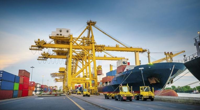 Modern Port Logistics with CHESSCON A cargo ship in a container terminal being unloaded by large yellow cranes while transport vehicles move containers.
