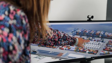 Digital Twins in Action with CHESSCON Live View A woman pointing at a screen displaying a 3D visualization of a container terminal represented as a digital twin.